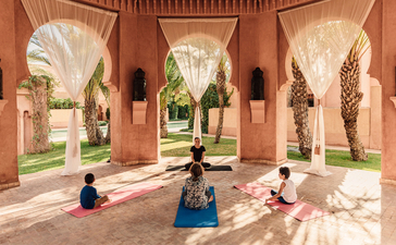 Famille pratiquant le yoga dans l'arcade en arches de la résidence Amanjena, au Maroc.