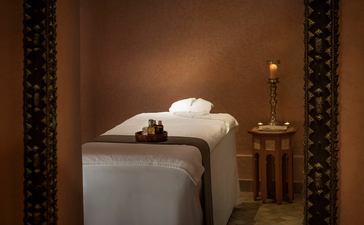 Spa treatment room at Amanjena with massage bed, folded towels, and warm candlelit ambience.