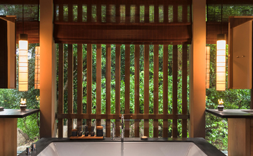 Amanoi entrance hall with wooden slat doors, warm lighting, and potted plants flanking the doorway.