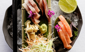 Amanoi dining: plated Asian dish with noodles, vegetables and seafood, garnished with lime slice and chopsticks.