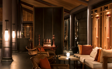 Amanoi lounge with warm wooden interiors, terracotta seating, and soft natural light filtering through architectural details.