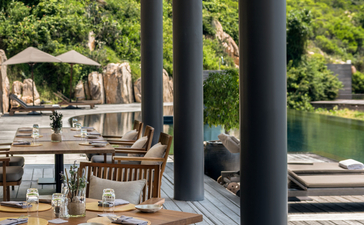 Wooden deck at Amanoi with dining furniture and water views through supporting columns.
