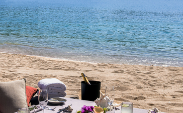 Beachfront dining setup at Amanoi with turquoise waters and forested hills beyond.