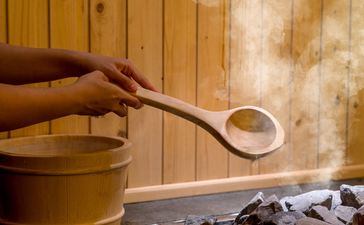 Hand pouring soup from brass ladle into bowl at Amanoi, with dried herbs and wooden backdrop.