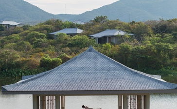 Amanoi pavilion with conical roof overlooking a lagoon and forested mountains in Vietnam.