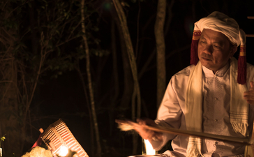 Woman seated by candlelit campfire at Amanoi, reading by firelight at night.