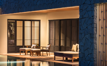 Amanoi villa with illuminated plunge pool at dusk, featuring wooden pavilion and stone facade.