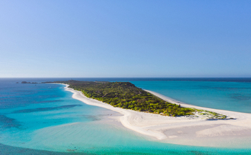 Aerial view of Amanpulo resort showing a pristine white-sand beach and turquoise waters surrounding a verdant island.