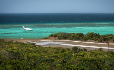 安缦璞乐度假村海岸线，绿松石色浅滩与翠绿植被相映，远处停泊一艘船只。