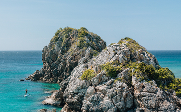 安缦璞乐度假村附近海域中，两座岩石岛屿被翠绿植被覆盖，周围碧蓝清澈的海水中点缀着游客。