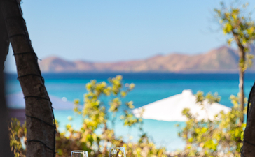 安缦璞乐度假村的餐桌眺望清澈海湾，树荫遮挡阳光。