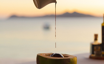 安缦璞乐度假村，手倒果汁入椰子杯，背景为晨雾笼罩的海景。