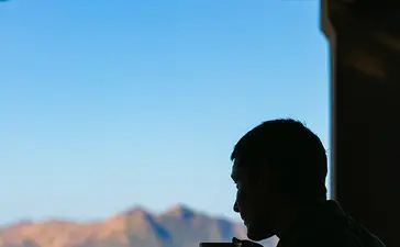 アマンプロ リゾートで、シルエットの人物がテラスから透き通った青い海と山々の景色を眺めている。