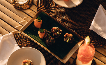 安缦璞乐度假村餐桌摆设，深色餐盘配白色餐巾，烛光晕染温暖氛围。