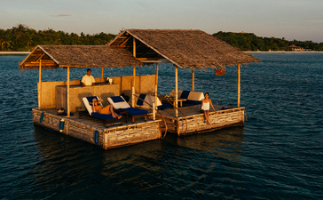 安缦璞乐度假村的木质浮台,坐落在宁静的蓝色海面上,金色阳光洒落其上。