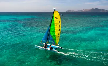 アマンプロのリゾートで、ターコイズブルーの海を帆走する黄緑色の帆のアウトリガーカヌー。