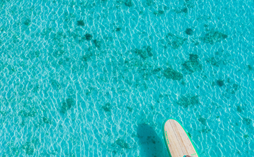 阿曼璞乐度假村，俯视图中一位客人在清澈碧蓝的海水中划桨冲浪。