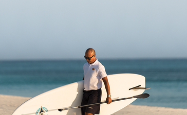 冲浪爱好者手持冲浪板走在安缦璞乐度假村的沙滩上，海洋在背景中。