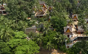Aerial view of Amanpuri resort nestled among tropical vegetation with traditional structures and a river below.