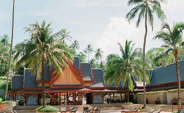 Amanpuri pool surrounded by palm trees and wooden pavilions at sunset.