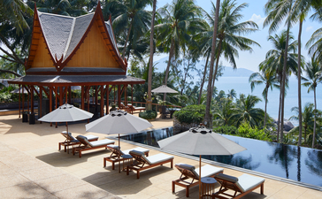 Amanpuri villa with teak pavilion, loungers and infinity pool overlooking palm-fringed beach.