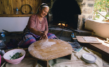 Woman preparing traditional bread at Amanruya, surrounded by cooking implements and ingredients.