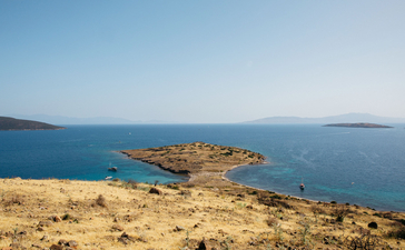 Amanruya's sandy coastline overlooks a small rocky island in clear blue Aegean waters.