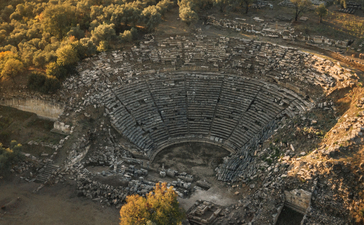 Aerial view of a circular stone amphitheatre surrounded by golden autumn vegetation at Amanruya.