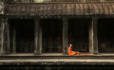 Buddhist monk in saffron robes sitting in meditation at Amansara, framed by ancient stone columns.
