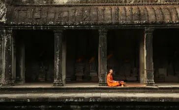 Buddhist monk in saffron robes sitting in meditation at Amansara, framed by ancient stone columns.
