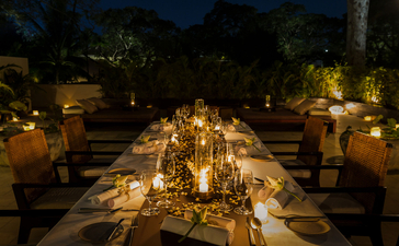 Candlelit dining table at Amansara stretches into the darkness, illuminated by warm golden light.