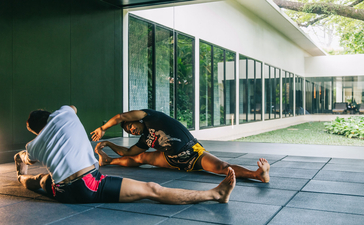 Yoga mats and props arranged on a sunlit terrace at Amansara, with verdant gardens visible through floor-to-ceiling windows.