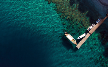 Aerial view of a wooden boat moored at Amanwana's jetty in clear turquoise waters.
