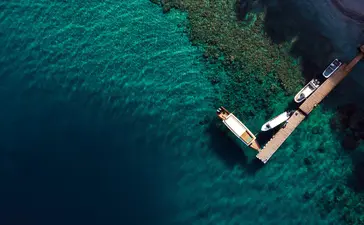 Aerial view of a wooden boat moored at Amanwana's jetty in clear turquoise waters.