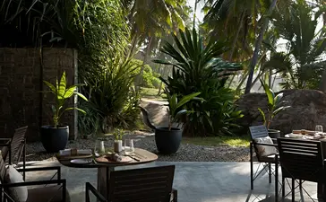 Amanwella's dining venue with stone terrace, dark tables and chairs, and lush tropical greenery surrounding the space.