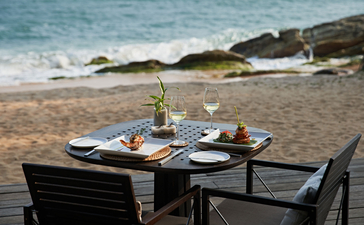 Dining table set on the beach at Amanwella, with place settings overlooking the ocean.