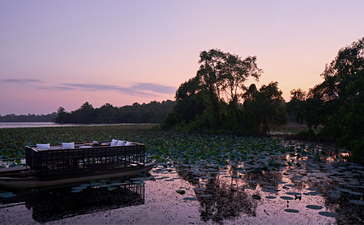 Amanwella's wetlands at dawn, with still water reflecting a soft purple sky and silhouetted trees along the horizon.