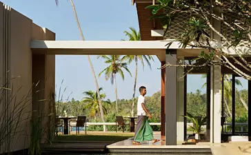 Amanwella villa with wooden pergola overlooking reflecting pool and palm trees.