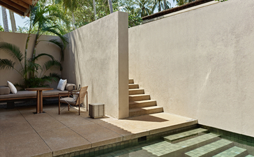 Courtyard at Amanwella with stone steps, seated figure, and planted palms.