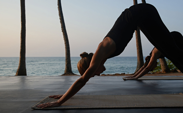 Woman in downward dog pose on wooden platform overlooking the sea at Amanwella wellness retreat.