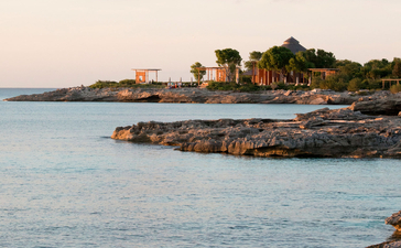 Côte rocheuse d'Amanyara avec plage de sable rose et eaux turquoise au crépuscule.