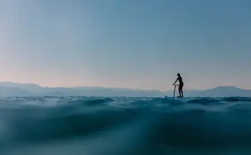 安缦卓熠度假村中，一位游客在清澈碧蓝的海水中独自站立，远处山峦轮廓依稀可见。