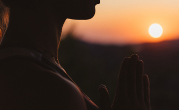 Silhouetted figure gazing towards sunset at Amanzoe, golden light reflecting on skin against darkening sky.