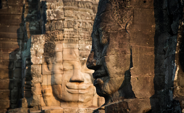 Stone carved face at Angkor, with serene expression emerging from weathered temple walls.