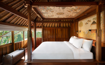 Ayung Suite bedroom at Amandari resort, featuring a four-poster bed with white linens beneath exposed wooden beams and traditional architectural details.