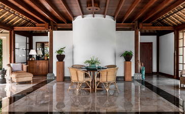 Ayung Suite living area at Amandari resort, featuring polished stone floors, wooden ceiling beams, and minimal furnishings with views to gardens.