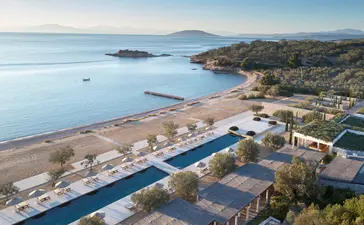Amanzoe's beachfront resort at dusk, with infinity pool overlooking calm Aegean waters and surrounding coastline.