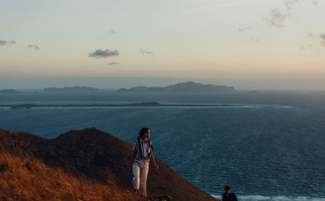 アマンプロ・リゾートの崖の上に立つ人物が、夕暮れ時の海を眺めている。