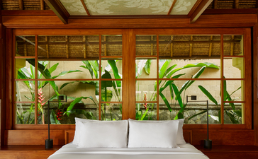 アマンダリ リゾートのバレー スイートの寝室。木製の窓枠越しに緑の植物が見える。