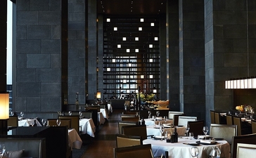 Dining venue at Aman Tokyo with soaring ceilings, vertical lighting panels, and tables set for service.